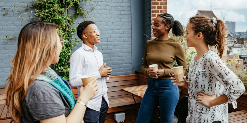 Four people are stood outside conversing holding coffees.