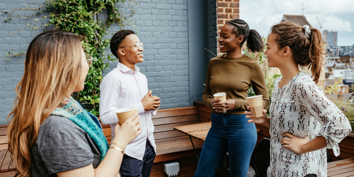 Four people are stood outside conversing holding coffees.