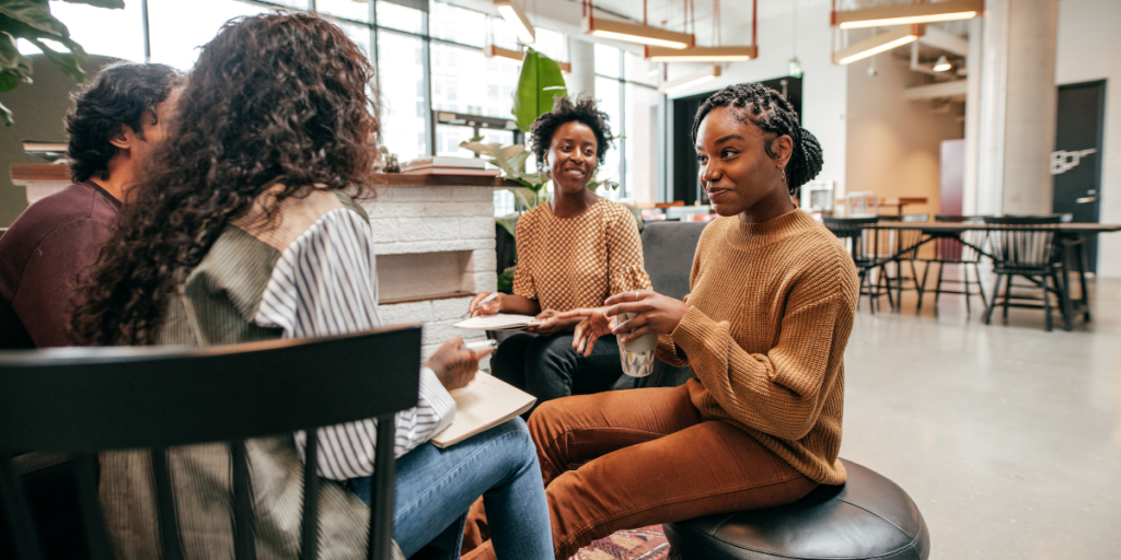 Four people sat in a circle in an office conversing.