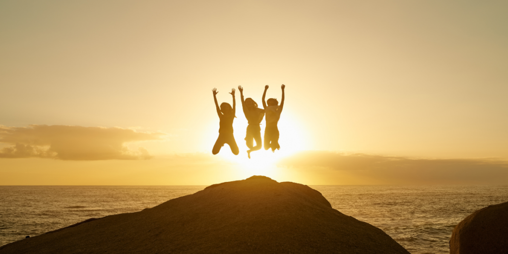Three people jumping in the air during sunset near the ocean.
