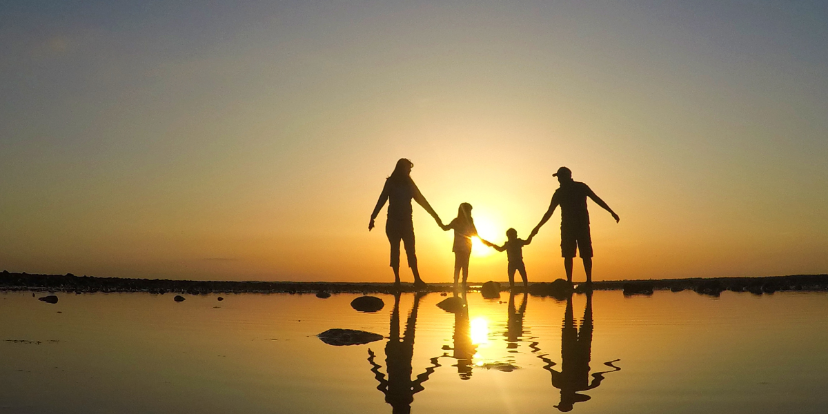 A family walking at the beach with the sunset reflecting their shadows in the water.