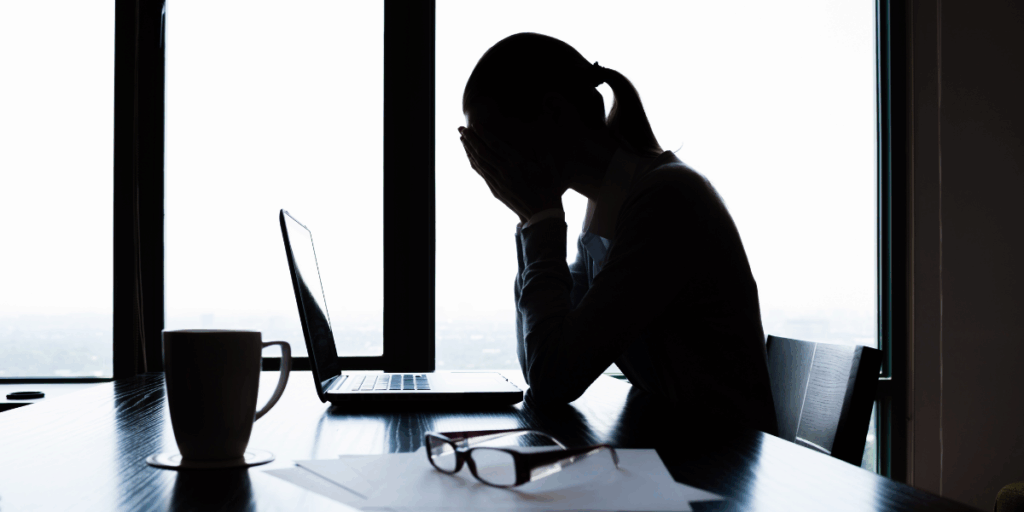 A woman is sat at a desk holding her hands over her face.