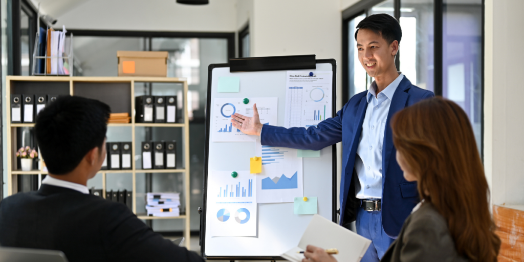 A man standing in front of a chart with financial data presenting to a team.