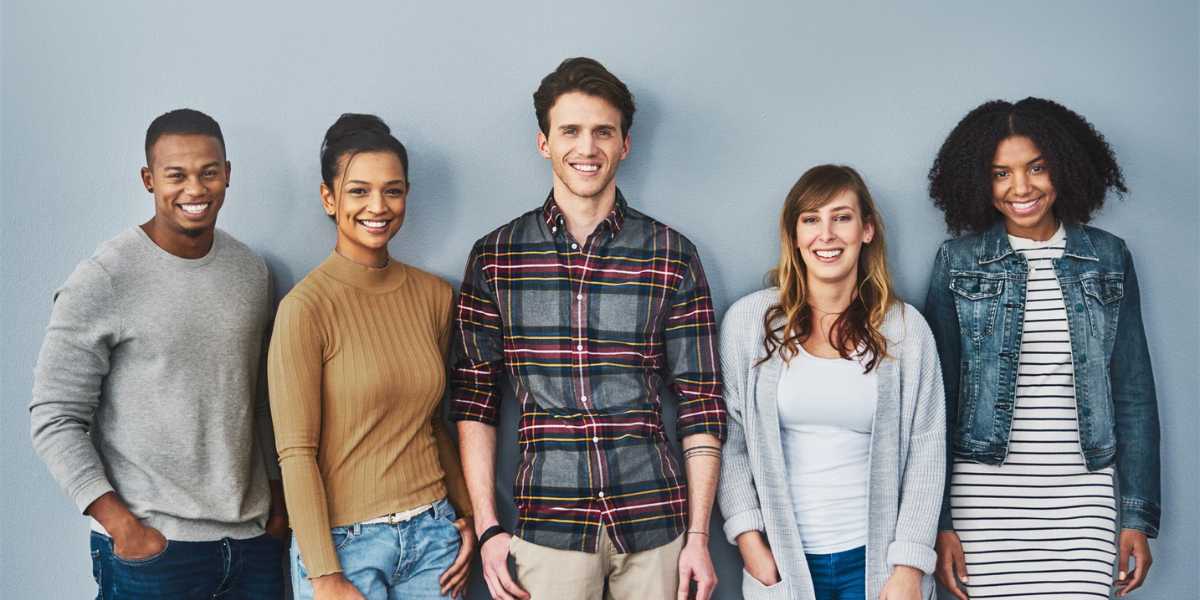 A group of five people standing against a grey wall smiling at the camera.