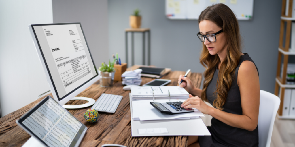 A woman is sitting at a desk writing notes and reviewing financial documents.