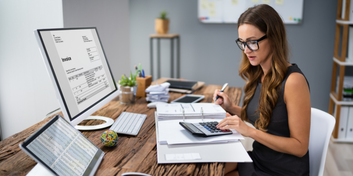 A woman is sitting at a desk writing notes and reviewing financial documents.