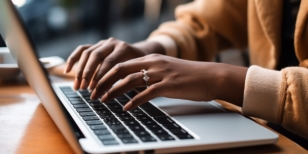 A woman is typing on her laptop which is resting on a wooden desk.