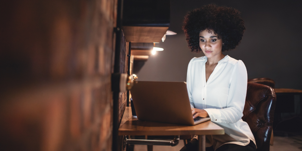 Woman sitting in dimly lit office working on laptop.