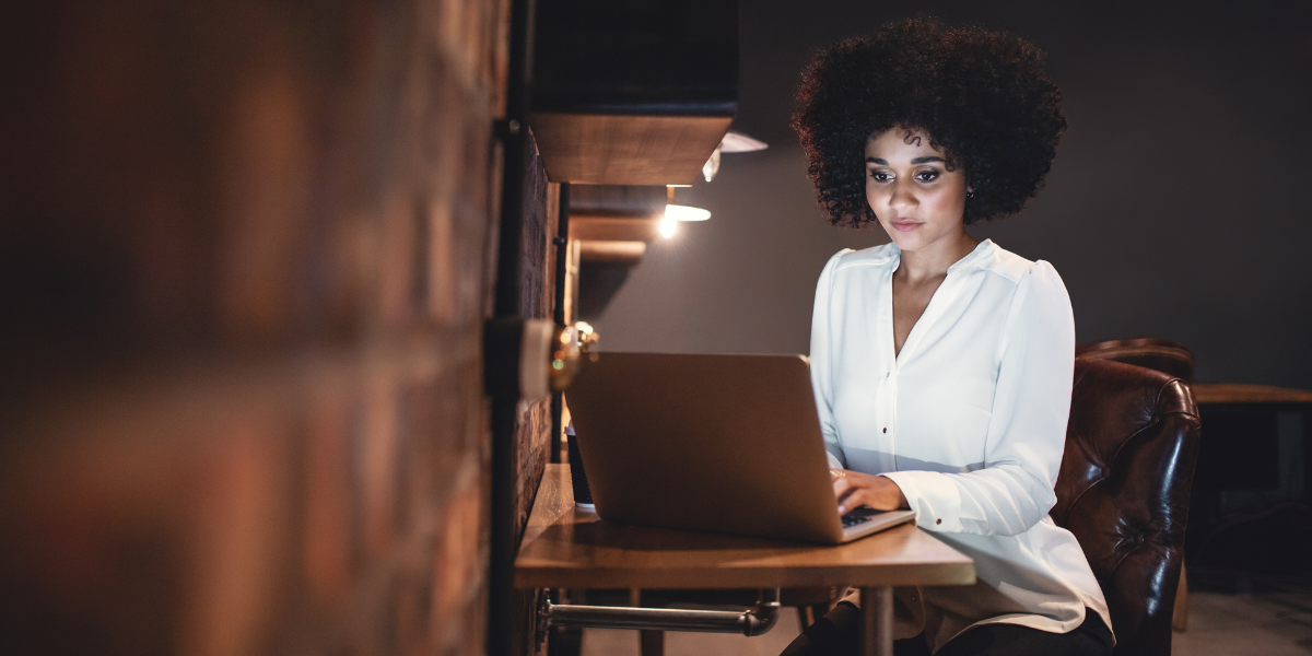 Woman sitting in dimly lit office working on laptop.