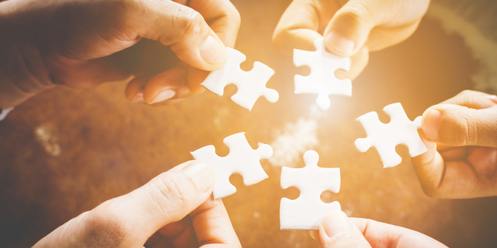 Four hands are holding puzzle pieces together.