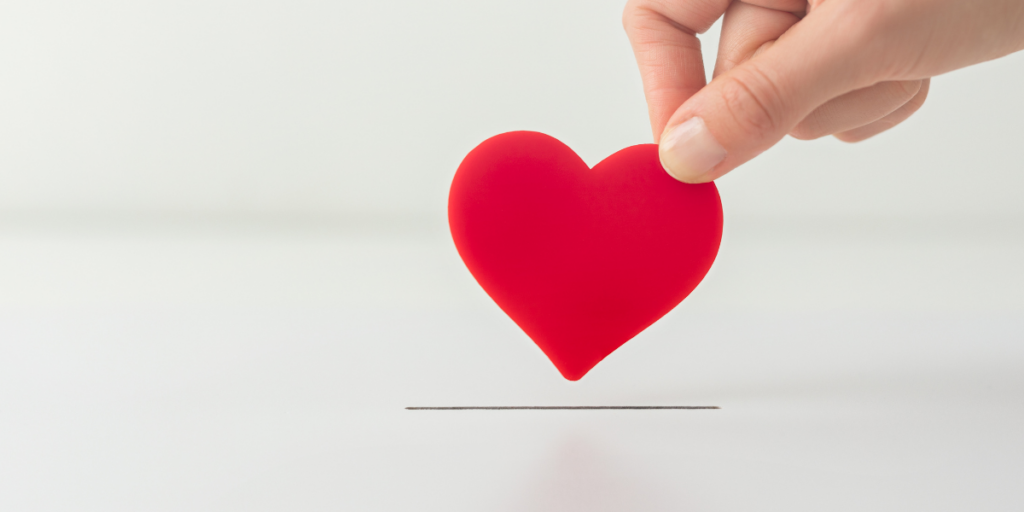 A hand is holding a red foam heart above a slot in a white box.