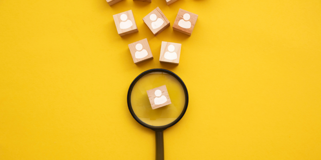 A yellow backdrop with a black magnifying glass and blocks with images of stick figures representing candidates. The magnifying glass has one candidate magnified.