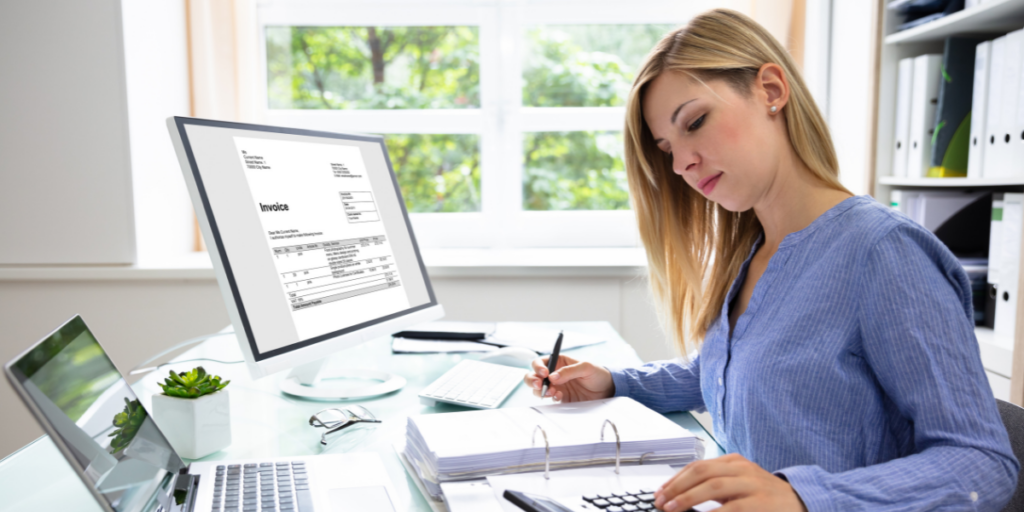A woman sitting at her desk reviewing accounting documents and writing notes.