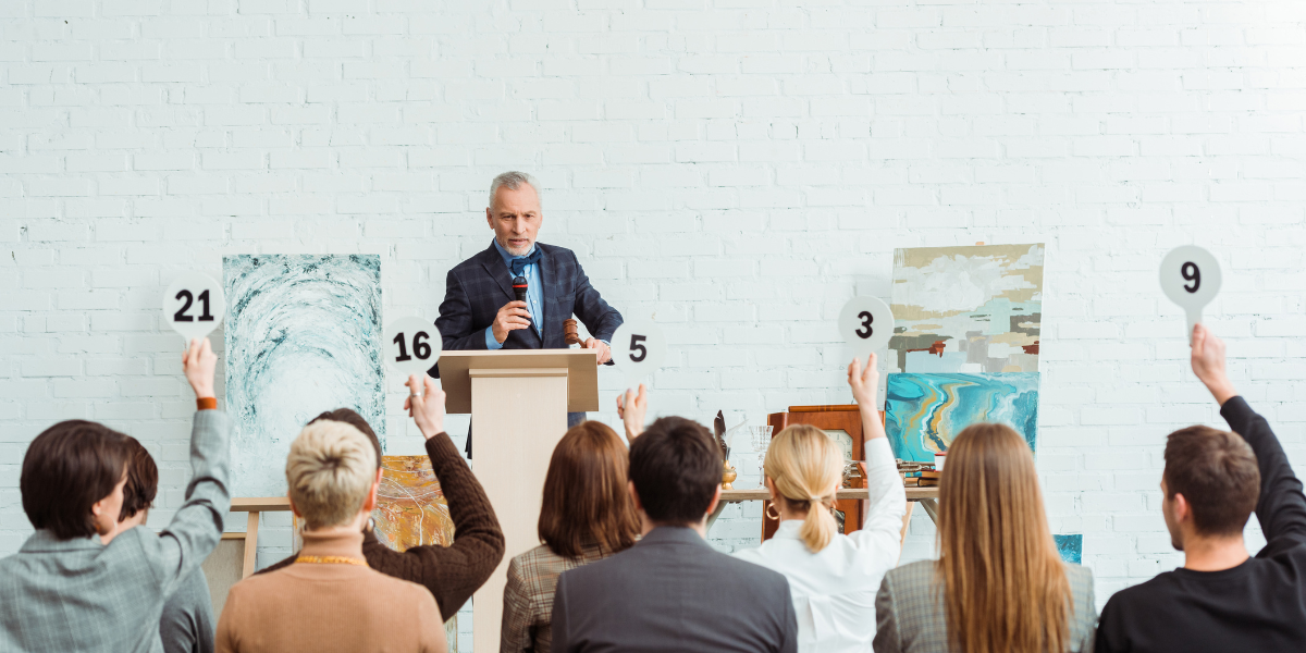 An auctioneer facilitating an auction for paintings. The audience is bidding on the auction items.