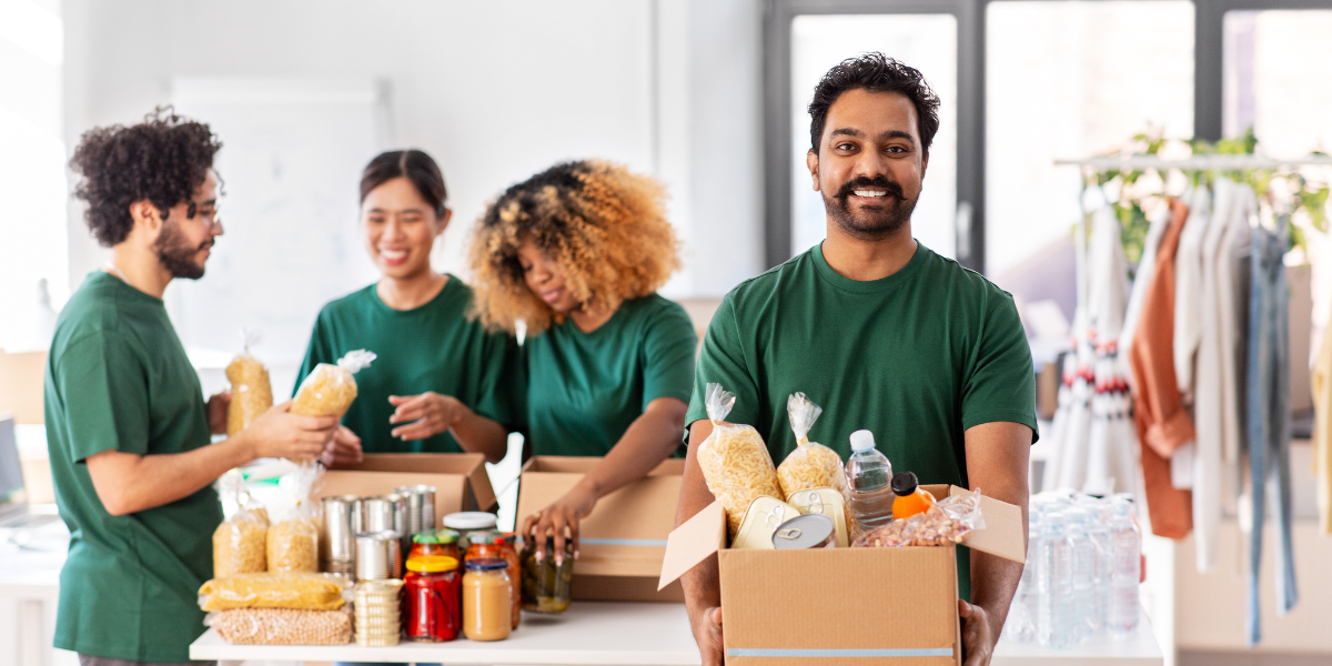 Four people volunteering at a food bank. A man is holding a box of donated food and looking at the camera.