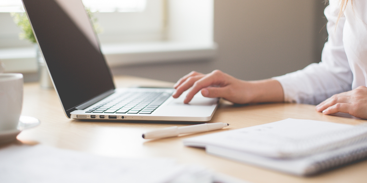 A woman is sat at her laptop on a wooden desk typing.