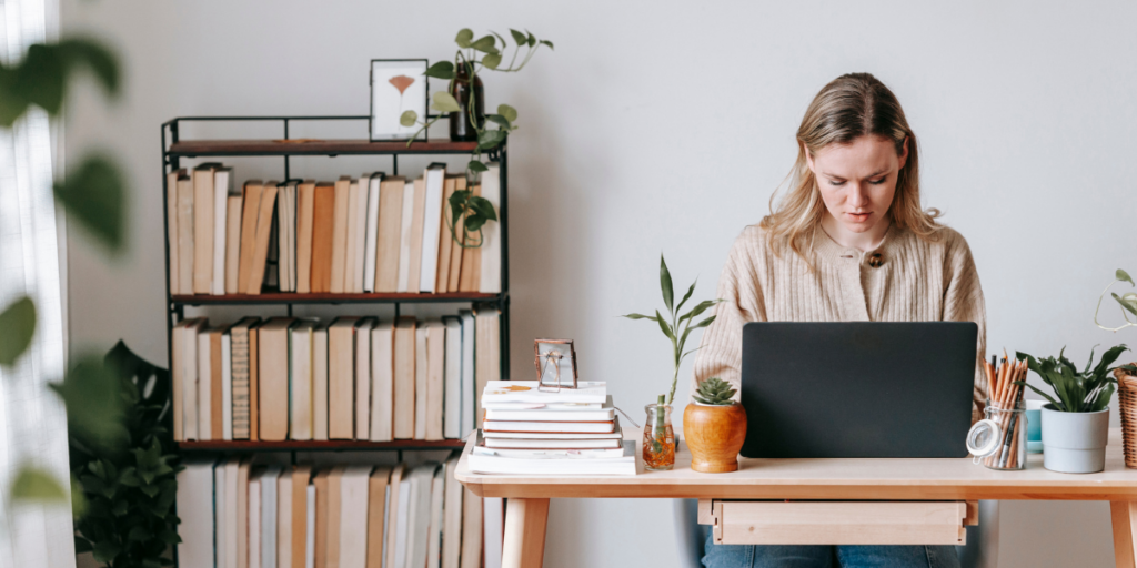 A woman sitting in her office typing. The room includes a bookcase and a plant.