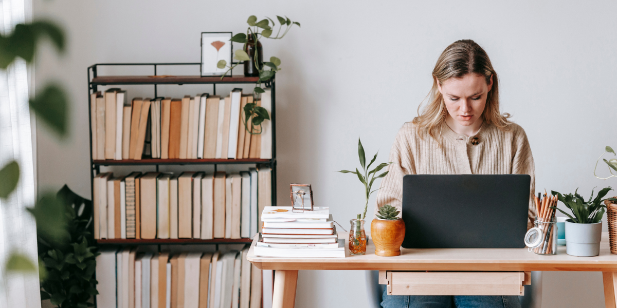 A woman sitting in her office typing. The room includes a bookcase and a plant.