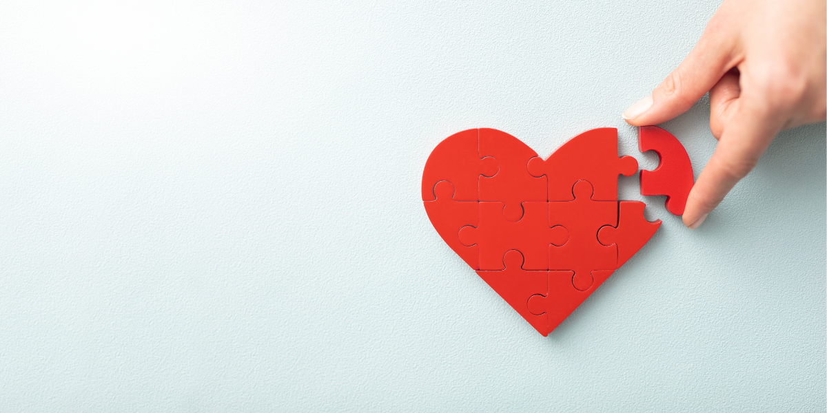 A red heart puzzle with a hand placing the last piece on a blue backdrop.
