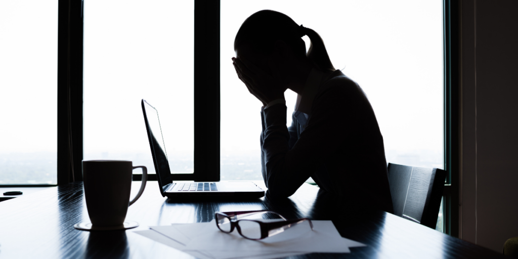 A woman is sitting at a desk with her head in hands.