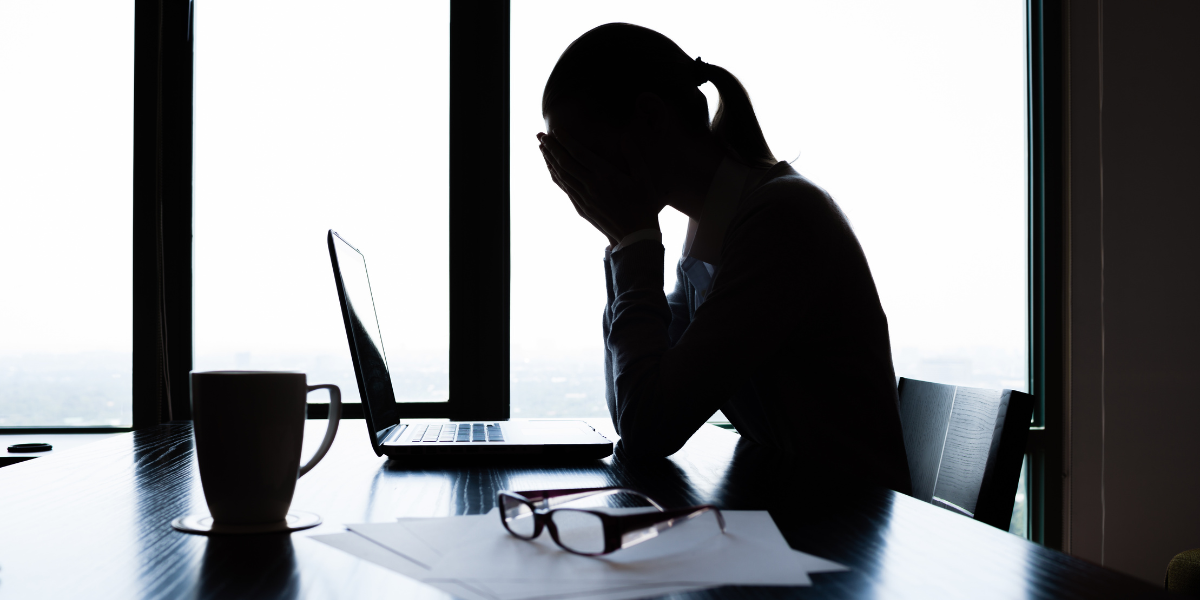 A woman is sitting at a desk with her head in hands.