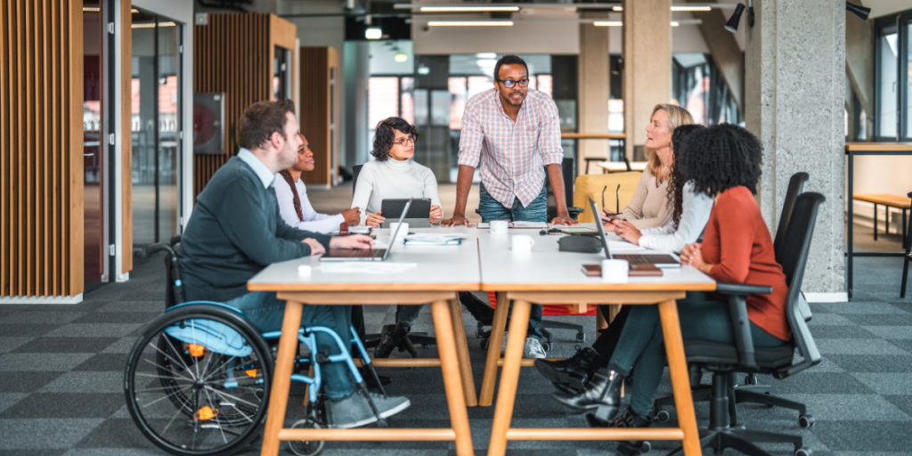 People sitting in a board room, and a man is standing at the table presenting.