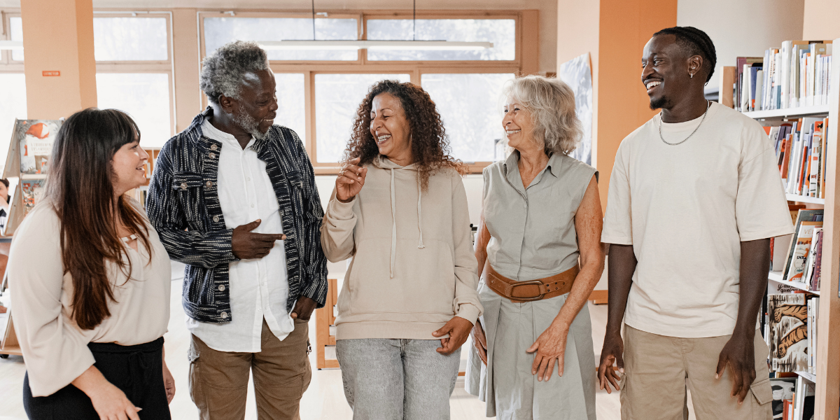 A group of five people standing in a line in a library conversing and laughing.