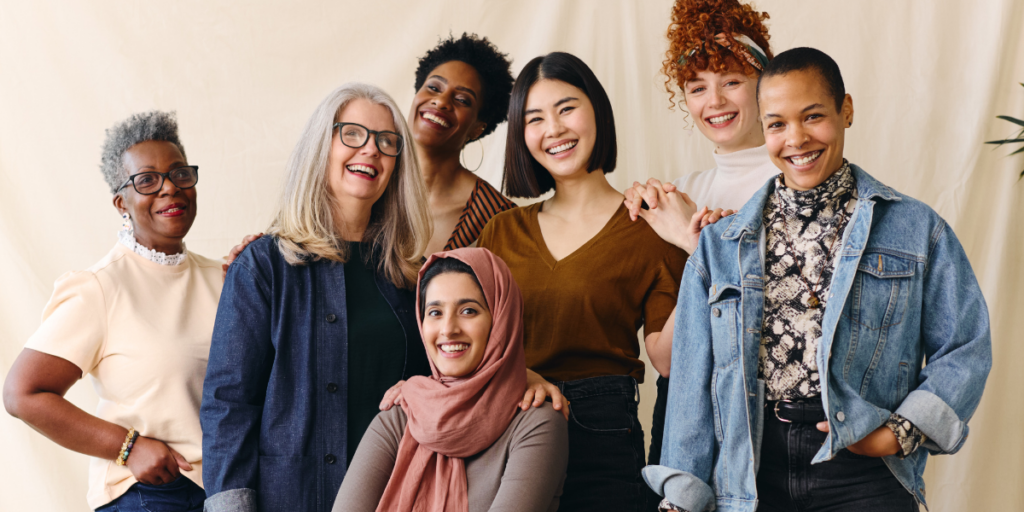 A group of women gathered together in front of a white backdrop smiling at the camera.