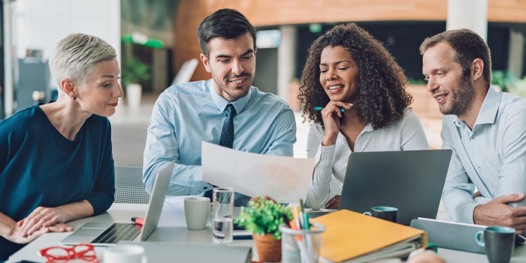 A group of four individuals are sat at a boardroom table reviewing documents.