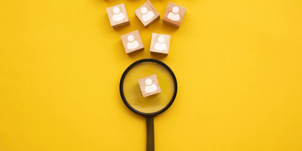 A yellow backdrop with a black magnifying glass and blocks with images of stick figures representing candidates. The magnifying glass has one candidate magnified.