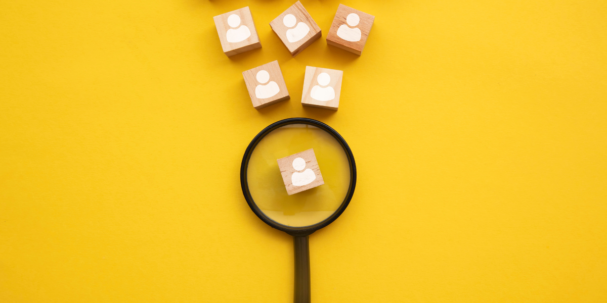 A yellow backdrop with a black magnifying glass and blocks with images of stick figures representing candidates. The magnifying glass has one candidate magnified.