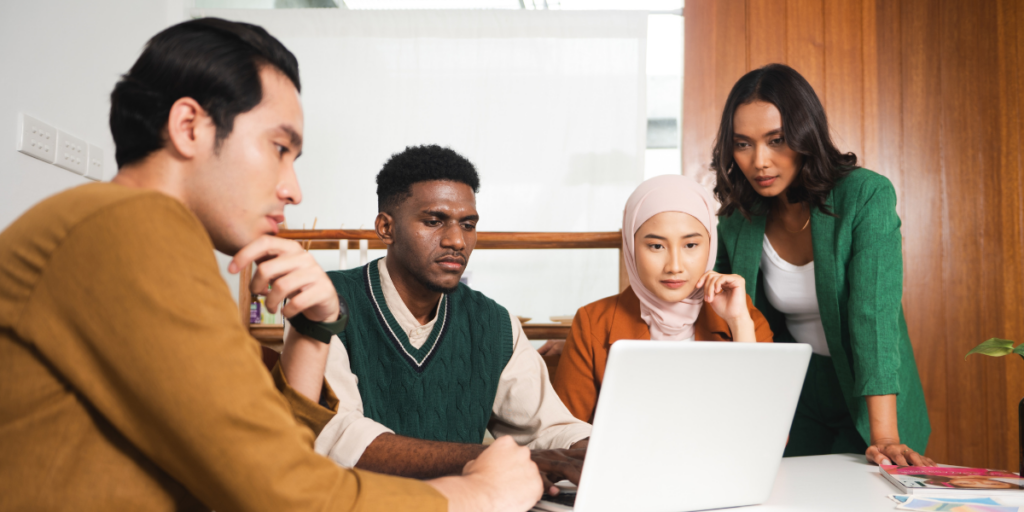Four people are sat at a boardroom table reviewing a laptop screen.