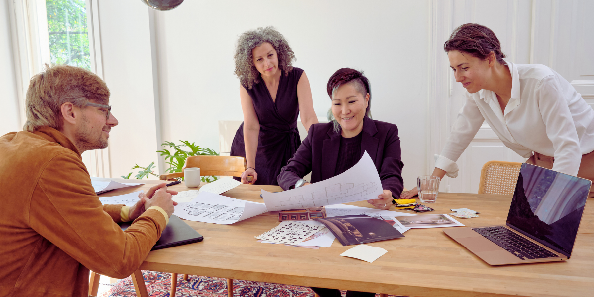 A group of people are sat at a boardroom table and reviewing a large document.