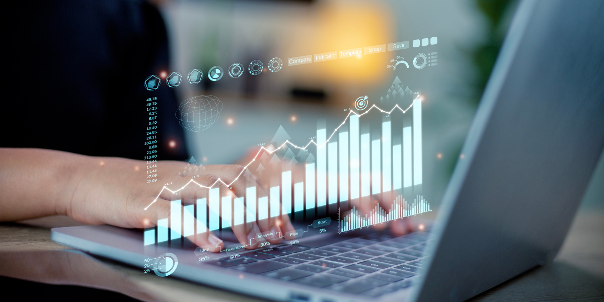 A person is typing on a laptop and a holograph bar graph is hovering over the keyboard.