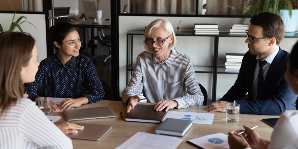 A group of people are sat at a boardroom table meeting and discussing.