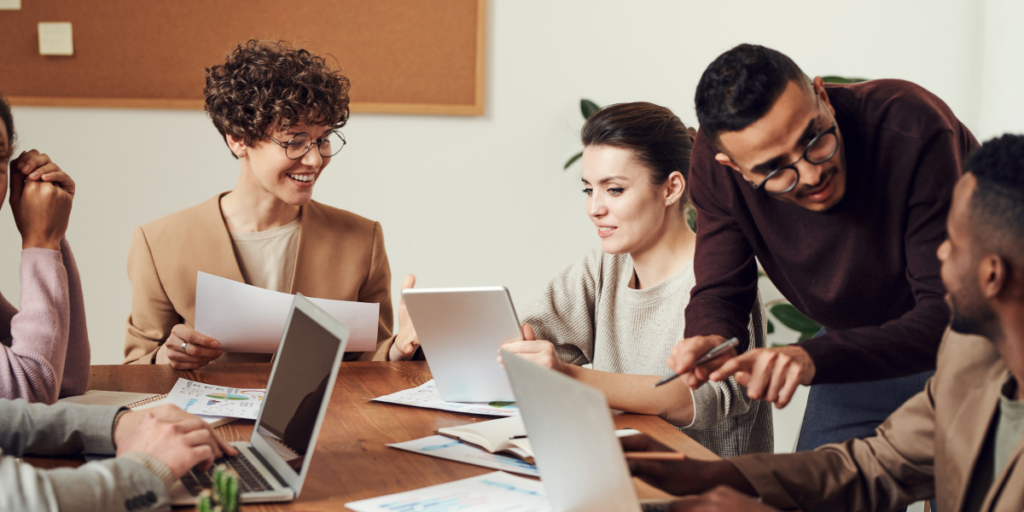 A group of people sitting at a boardroom table conversing and reviewing notes.