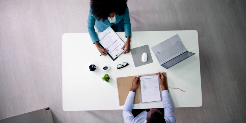 Two people are sat at a board room table reviewing paperwork.