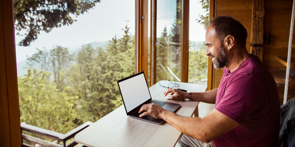 A man sitting at a desk typing in front of a picture window.
