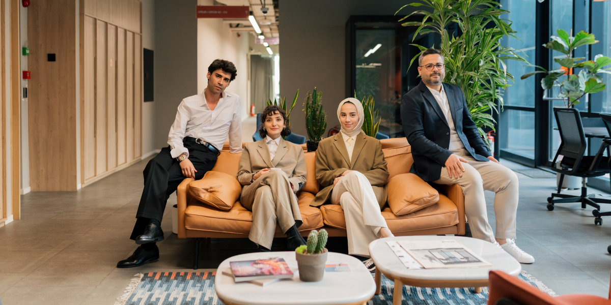 A group of people are sat on a couch in an office space facing the camera and smiling.