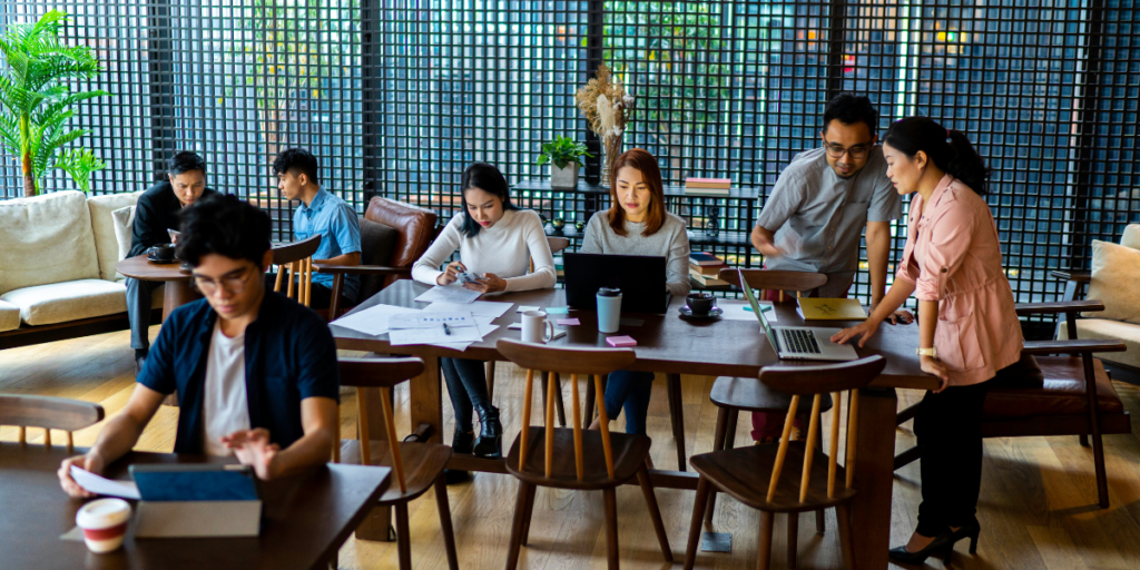 An office of people are sat at different workspaces collaborating and working on projects.