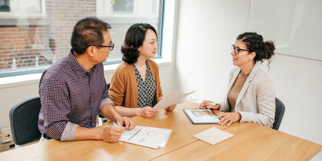 Three people sat at a boardroom table discussing and reviewing a tablet.