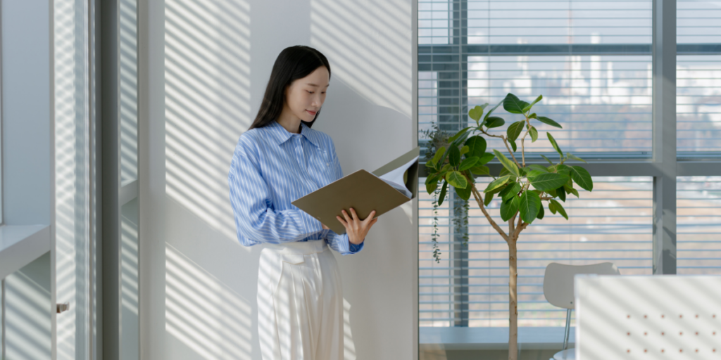 A woman is stood in a well-lit room holding a file folder.