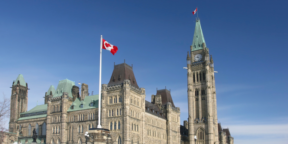 The Government of Canada parliamentary building and a Canadian flag flying.