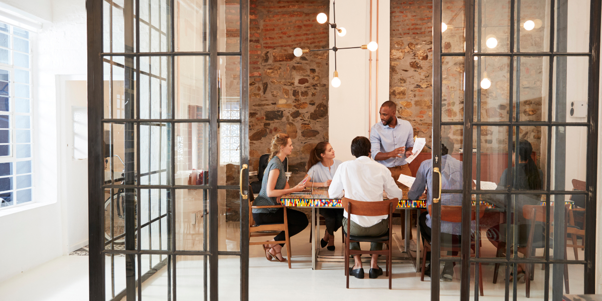 A board of people are sat looking at a man speaking and holding a piece of paper.