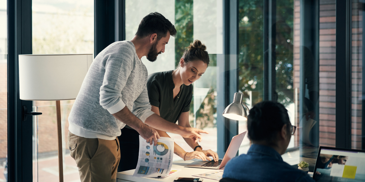 Three people are huddled around an office desk collaborating.