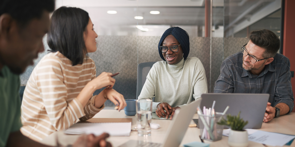 A group of individuals are sat at a boardroom table in a bright room.