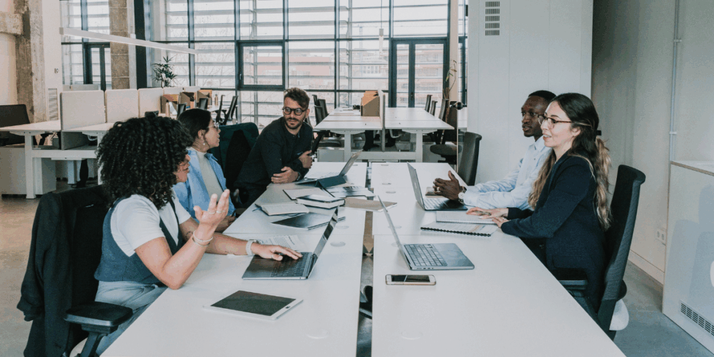 A boardroom with five people sitting at the boardroom table conversing.