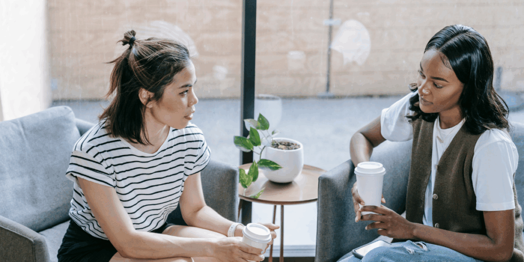 Two women are sat in armchairs conversing.