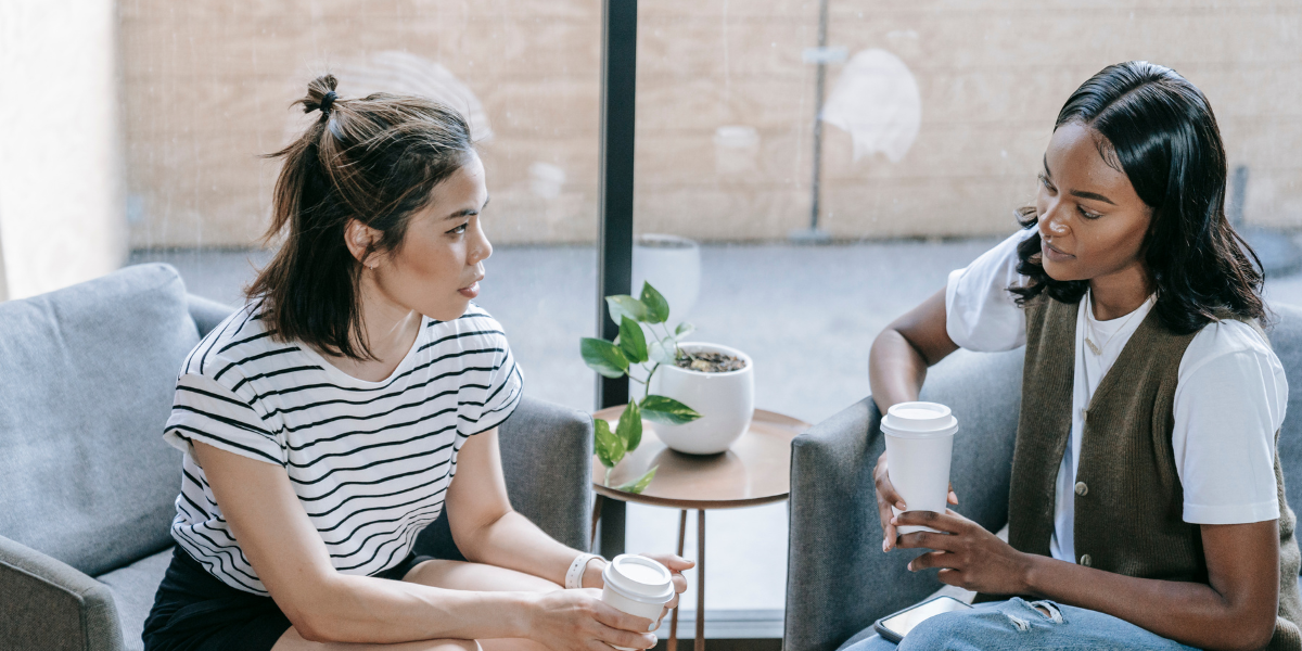 Two women are sat in armchairs conversing.
