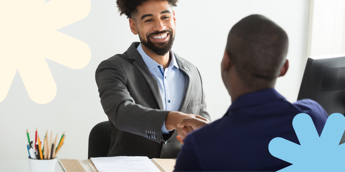 A person is sat facing another individual and they are shaking hands.